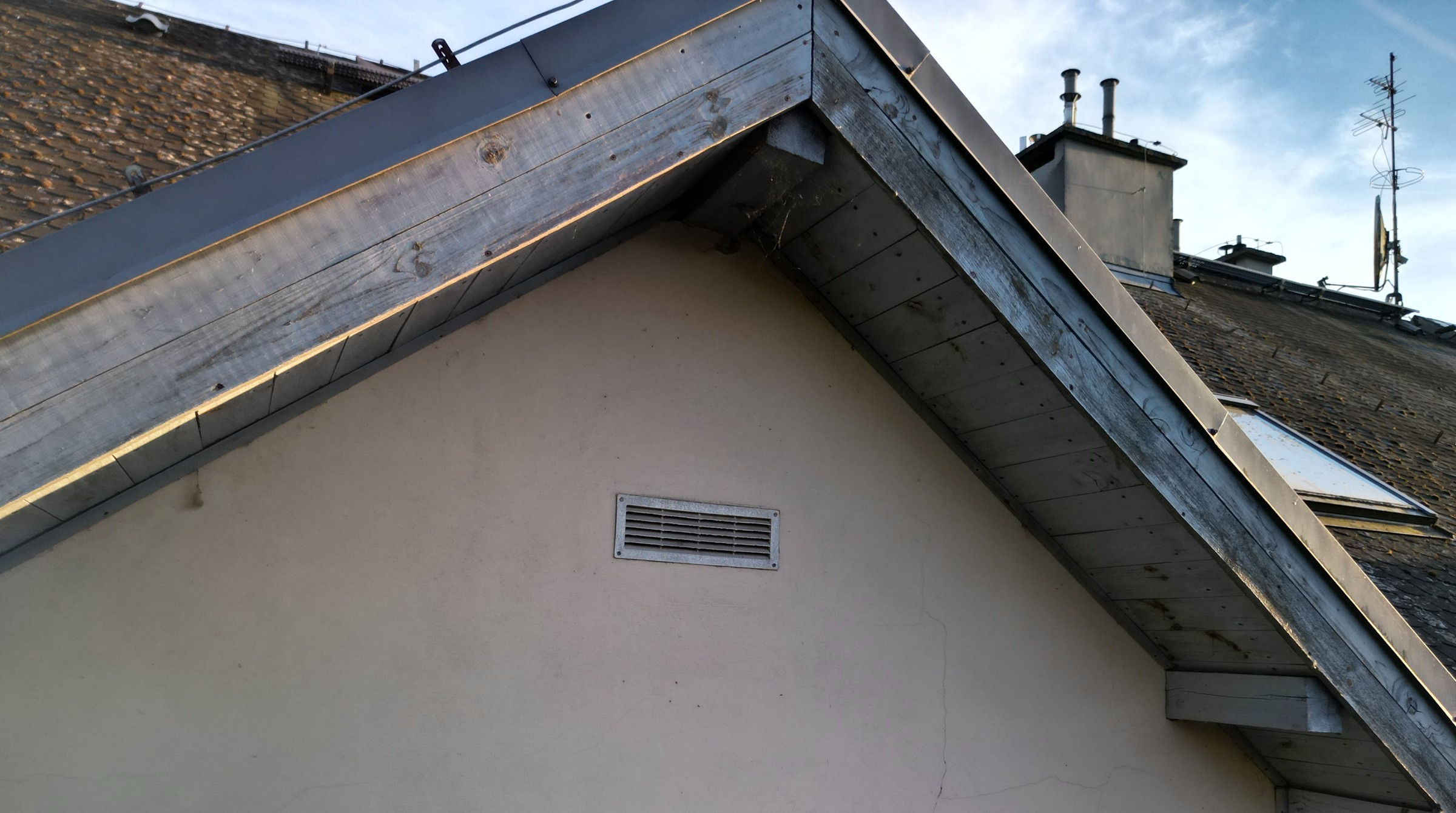 Building gable with grey timber boards; fine cracks are visible in the light-coloured render below the gable.