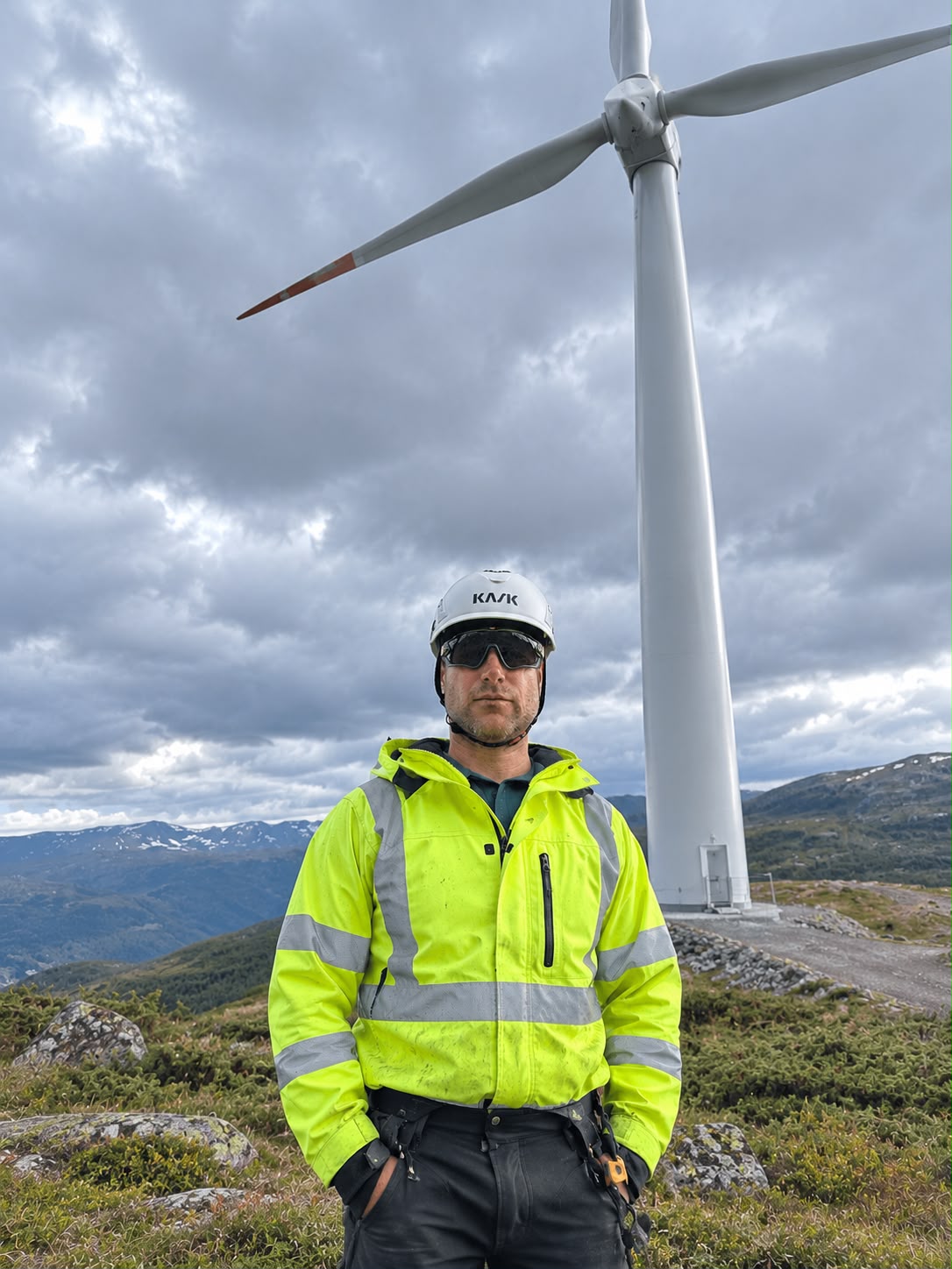 Paweł Jedliński from Aeronautiq in high-visibility protective clothing and a safety helmet in front of a wind turbine